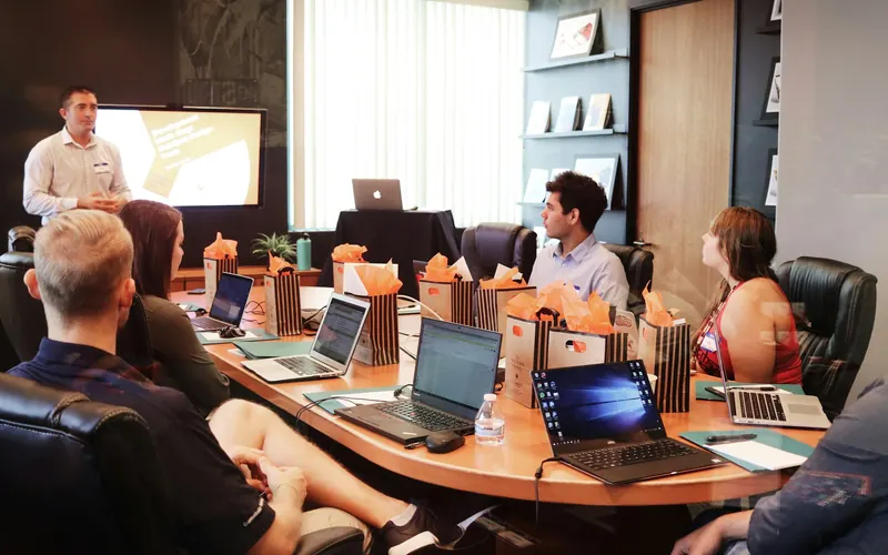 A presenter talking to a team around a table with laptops