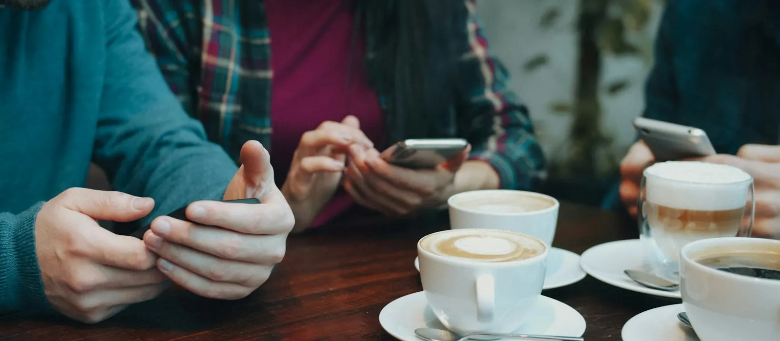 Three people using smartphones at a table with cups of coffee