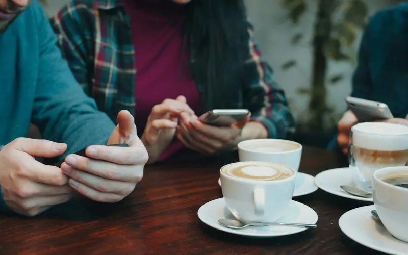 Three people using smartphones at a table with cups of coffee