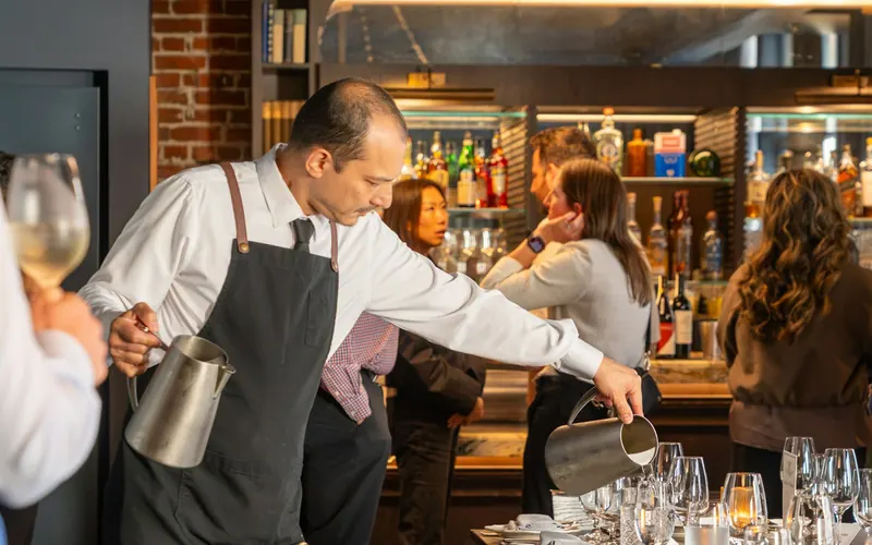 A server in a black apron pouring water at a restaurant table