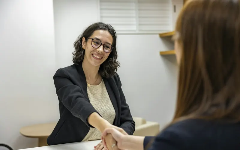 Two women shaking hands across a table at an interview